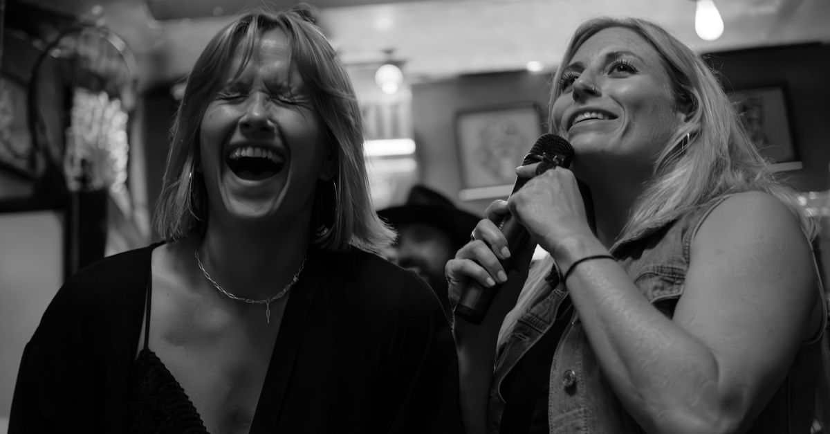 Two women laughing and singing at a karaoke night, exuding joy and camaraderie.